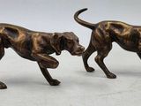 two bronze figurines of dogs running on a white surface
