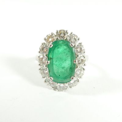 un gros plan d'une bague sertie d'une émeraude verte et de diamants sur fond blanc