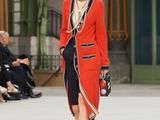 the woman is walking down the runway wearing a red coat