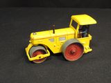 a yellow toy tractor with a roller on a black surface