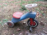 un petit tricycle bleu avec un siège rouge posé par terre
