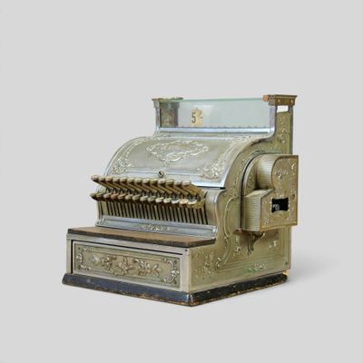 a silver and gold cash register sitting on a white surface