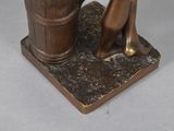 bronze statue of a woman sitting on a stool next to a wooden barrel