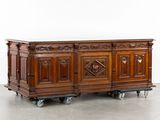 un buffet ancien en bois monté sur roulettes, orné de sculptures sur le dessus