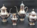 three silver teapots and two silver cups on a table