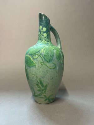 un vase vert posé sur une table près d'un mur blanc