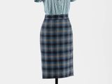 une robe posée sur un présentoir à mannequin, avec une chemise bleue et une jupe à carreaux