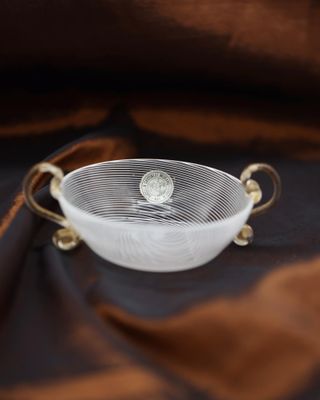 an image of a white bowl with gold handles on a brown cloth