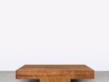 une table basse en bois avec un plateau carré, posée sur un sol en béton