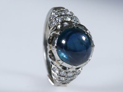 gros plan d'une bague avec une pierre bleue entourée de diamants