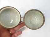 someone is holding two bowls in their hand on a white surface