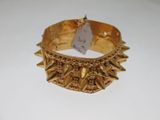 bracelet en or orné de pointes et d'une plaque, posé sur une surface blanche