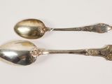 pair of silver spoons on a white surface with a white background