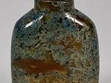 un vase vert et marron muni d'un couvercle, posé sur une surface blanche