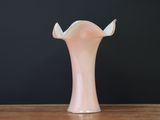 un vase rose posé sur une table en bois, avec un mur noir en arrière-plan