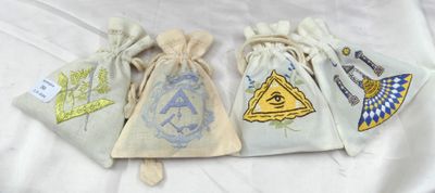 trois petits sacs à cordon ornés de symboles maçonniques, posés sur un lit