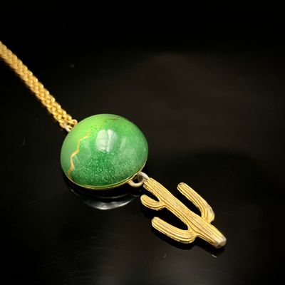 Collier plaqué or avec une pierre verte et un cactus sur fond noir