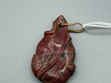 une photo d'un pendentif rouge en forme de feuille, suspendu à un cordon blanc