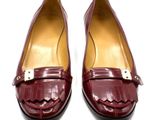 une paire de chaussures en cuir bordeaux ornées de boucles dorées sur un fond blanc