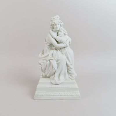 statue blanche représentant une femme tenant un enfant dans ses bras, posée sur un socle