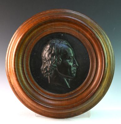 une photo d'un portrait en bronze représentant un homme, dans un cadre en bois