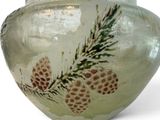 a glass vase with pinecones on it on a white surface