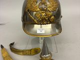 un casque argenté orné d'un aigle en or, à côté d'une paire de ciseaux