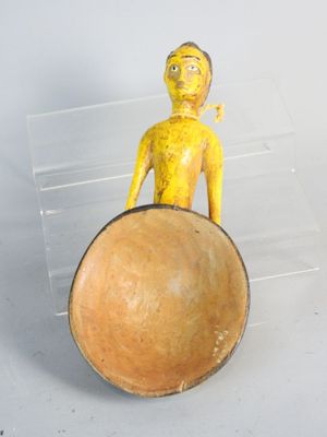 a small yellow figurine sitting on top of a wooden bowl