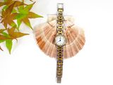 a watch sitting on top of a shell with a plant in the background