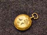 une petite montre de poche en or posée sur un tissu marron