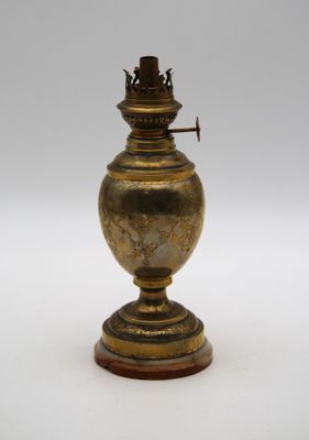 une lampe à huile ancienne en laiton posée sur un socle en bois, sur fond blanc
