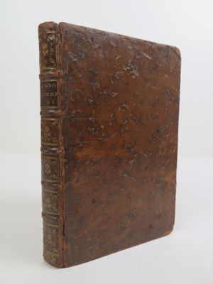 an old brown book sitting on top of a table next to a white wall