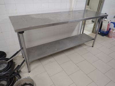 une table en acier inoxydable dans une cuisine où des casseroles et des poêles sont posées par terre