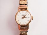 une montre-bracelet en or avec un cadran blanc sur une surface blanche