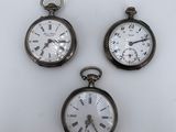 trois montres de poche anciennes posées sur une surface blanche