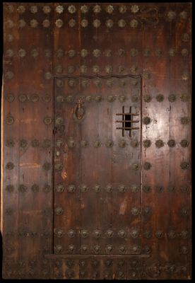 une vieille porte en bois avec des rivets métalliques et une petite fenêtre