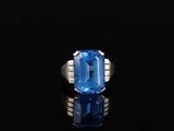 une bague en topaze bleue et diamants posée sur un fond noir