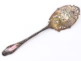 une cuillère en argent avec un manche rose posée sur une surface blanche