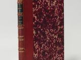 an old book with a red cover sitting on top of a white surface