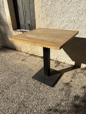 a wooden table with a black metal base on the sidewalk
