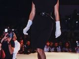 a woman in a black dress and white hat walking down the runway