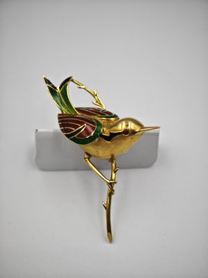 une image représentant une broche en forme d'oiseau doré posée sur une surface blanche