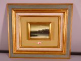 tableau représentant un paysage, encadré d'or, accroché à un mur blanc