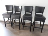 quatre tabourets de bar en cuir noir disposés devant un mur blanc