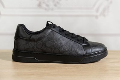 the black sneakers are on a wooden table with a white wall in the background