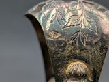 a close up of a silver vase with a bird on it