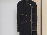 black coat with gold buttons hanging on a clothes rack in front of a beige wall