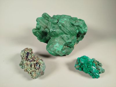 three pieces of green mineral sitting next to each other on a white surface