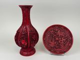 un vase rouge et une assiette placés l'un à côté de l'autre