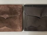 two brown and black wallets sitting on top of a white table